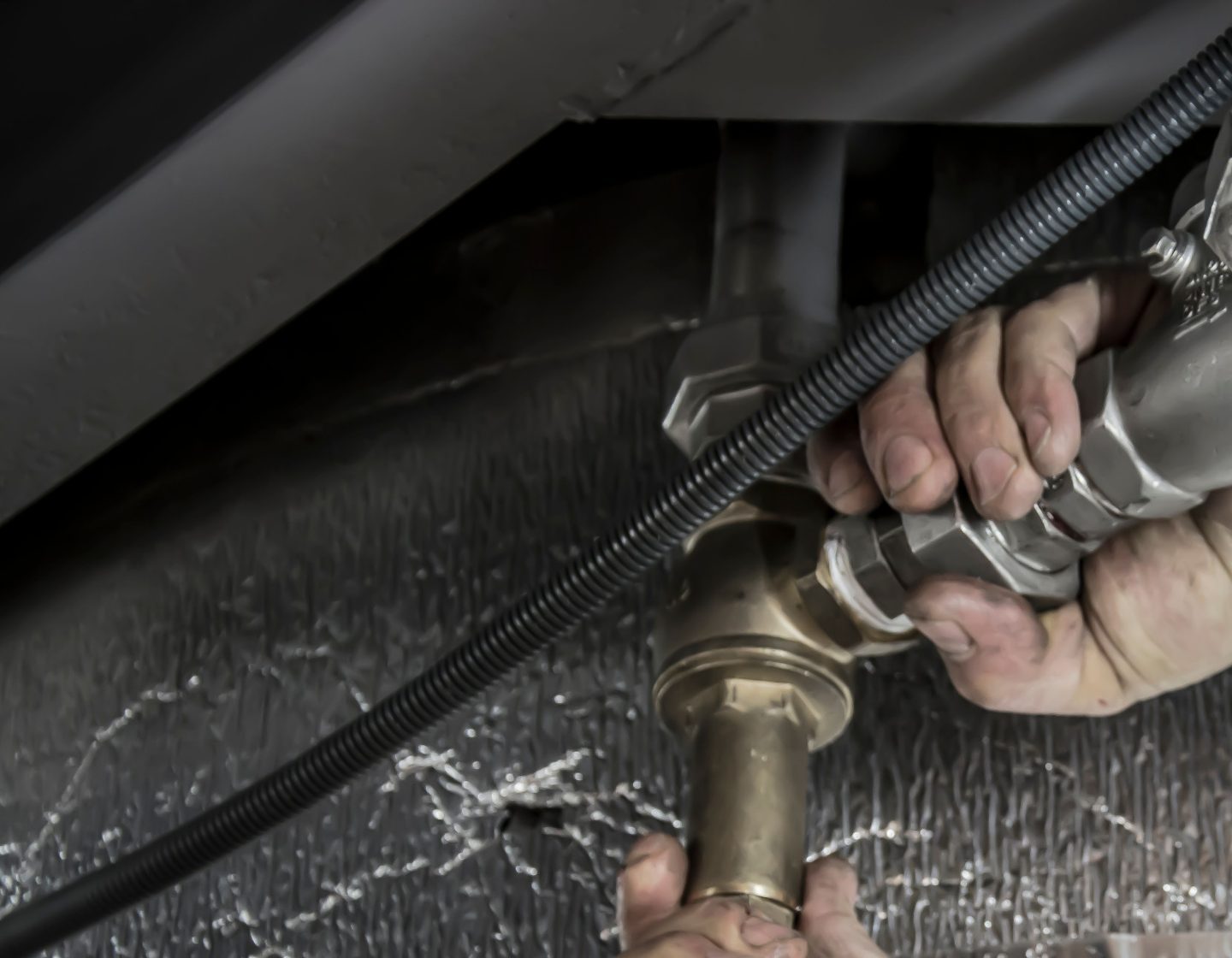 Close-up of a plumber's hands installing steel pipes indoors, showcasing skilled manual work.